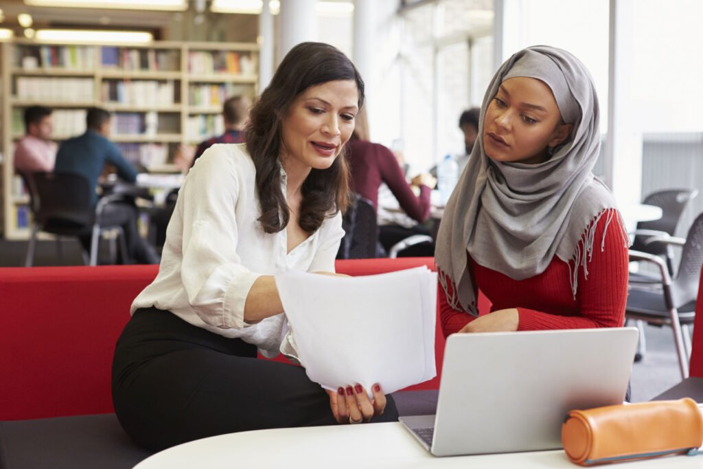 Female University Student Working In Library With Tutor